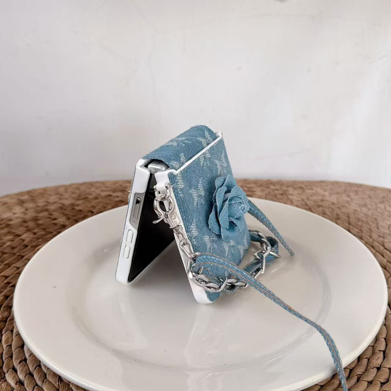Samsung Z Flip standing in flex mode on a ceramic plate protected by a blue denim flower wrist strap case.