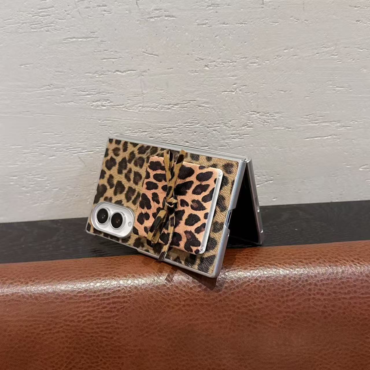 Semi-folded Samsung Galaxy Z Fold standing on a surface showcasing leopard print back cover and bow mirror accent