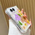 Side perspective view of a hand holding the clear iPhone DUO pressed flower case, displaying reinforced corner bumpers, precision side button alignment, and dual camera lens bezel.