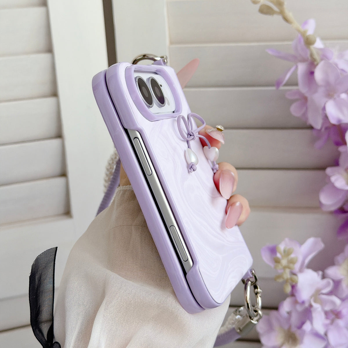 Side profile close-up of pastel lavender marble case for iPhone DUO held in hand, displaying the folding hinge frame construction and attached purple pearl lanyard strap.