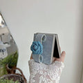 Side profile of partially open Samsung Z Flip phone displaying the 3D denim floral strap attachment.