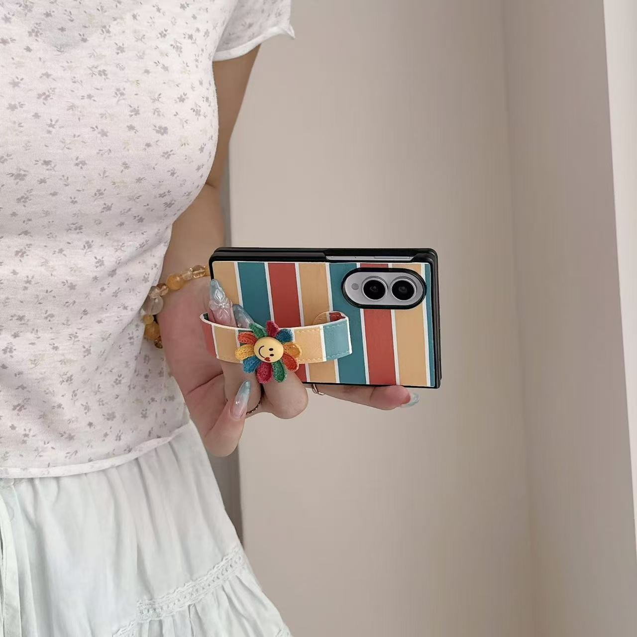 Side view of a hand securely holding a Samsung Galaxy Z Fold using the integrated rainbow stripe leather strap band with crocheted smiley flower