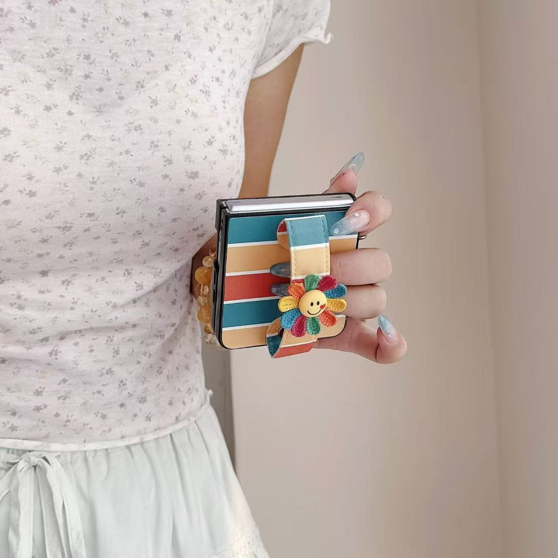 Side view of hand gripping a folded Samsung Z Flip phone using the integrated colorful flower hand strap