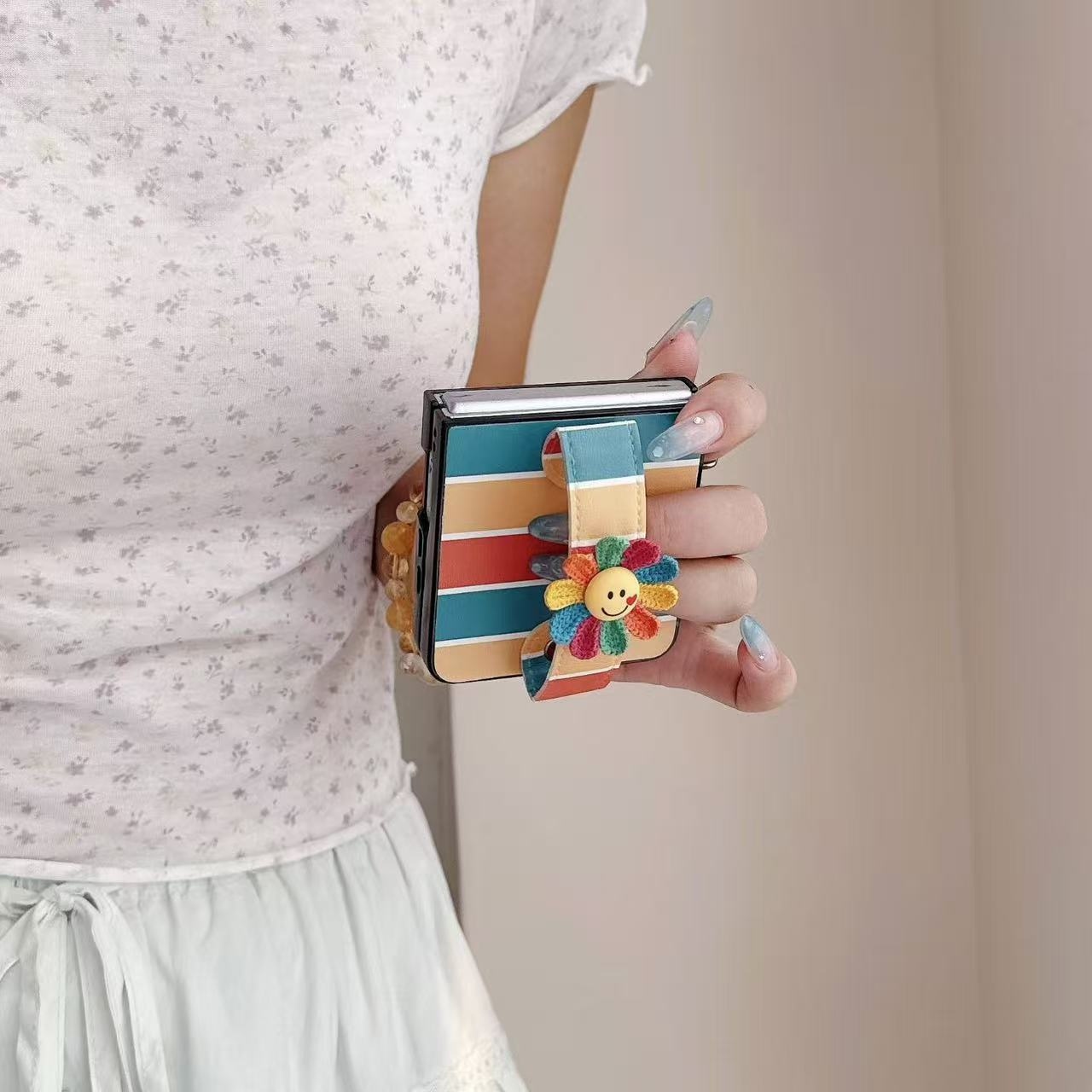 Side view of hand gripping a folded Samsung Z Flip phone using the integrated colorful flower hand strap