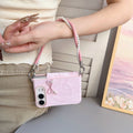 Soft blush pink marble swirl case for iPhone DUO worn as a wristlet handbag accessory showing the pearl bow charm and pink pearl-lined lanyard strap.