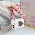 Soft blush pink polka dot case for iPhone DUO carried as a wristlet handbag accessory showing the crystal heart mirror and pink satin scrunchie bow strap.