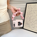 Soft blush pink polka dot case for iPhone DUO suspended by its pink satin scrunchie bow wristlet strap held in hand.