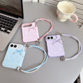 Three color variants of the iPhone DUO marble swirl cases in soft pink, sky blue, and lavender purple laid out on a table with matching pearl lanyard wristlet straps.