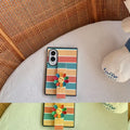 Top-down flat lay view of cute pastel rainbow striped Samsung Galaxy Z Fold case with smiley flower strap on a woven surface