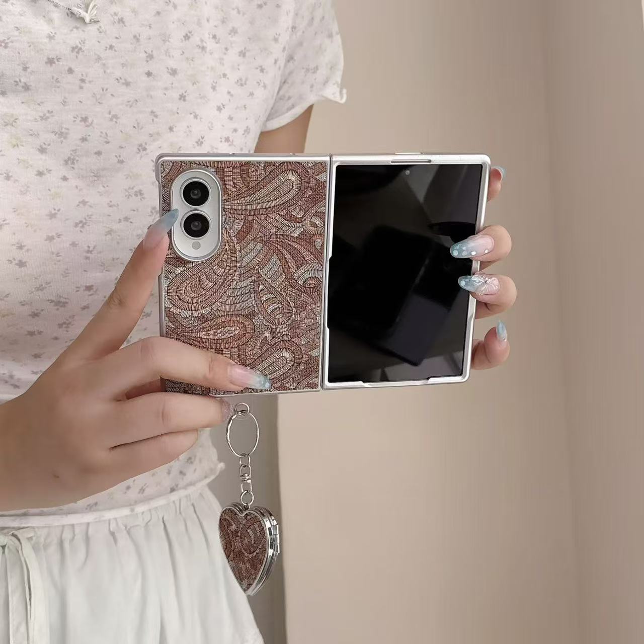 Unfolded Samsung Galaxy Z Fold 8 phone held in hands showing the inner display screen and brown paisley embroidered back cover.