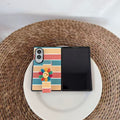 Top-down flat lay view of cute pastel rainbow striped Samsung Galaxy Z Fold case with smiley flower strap on a woven surface