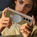 Woman holding a Samsung Galaxy Z Fold phone in a champagne gold glitter case connected to a magnetic wireless charger.