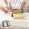 Yellow dual-tone leather iPhone DUO wallet case set up in horizontal hands-free desktop kickstand mode on a desk next to a reader.