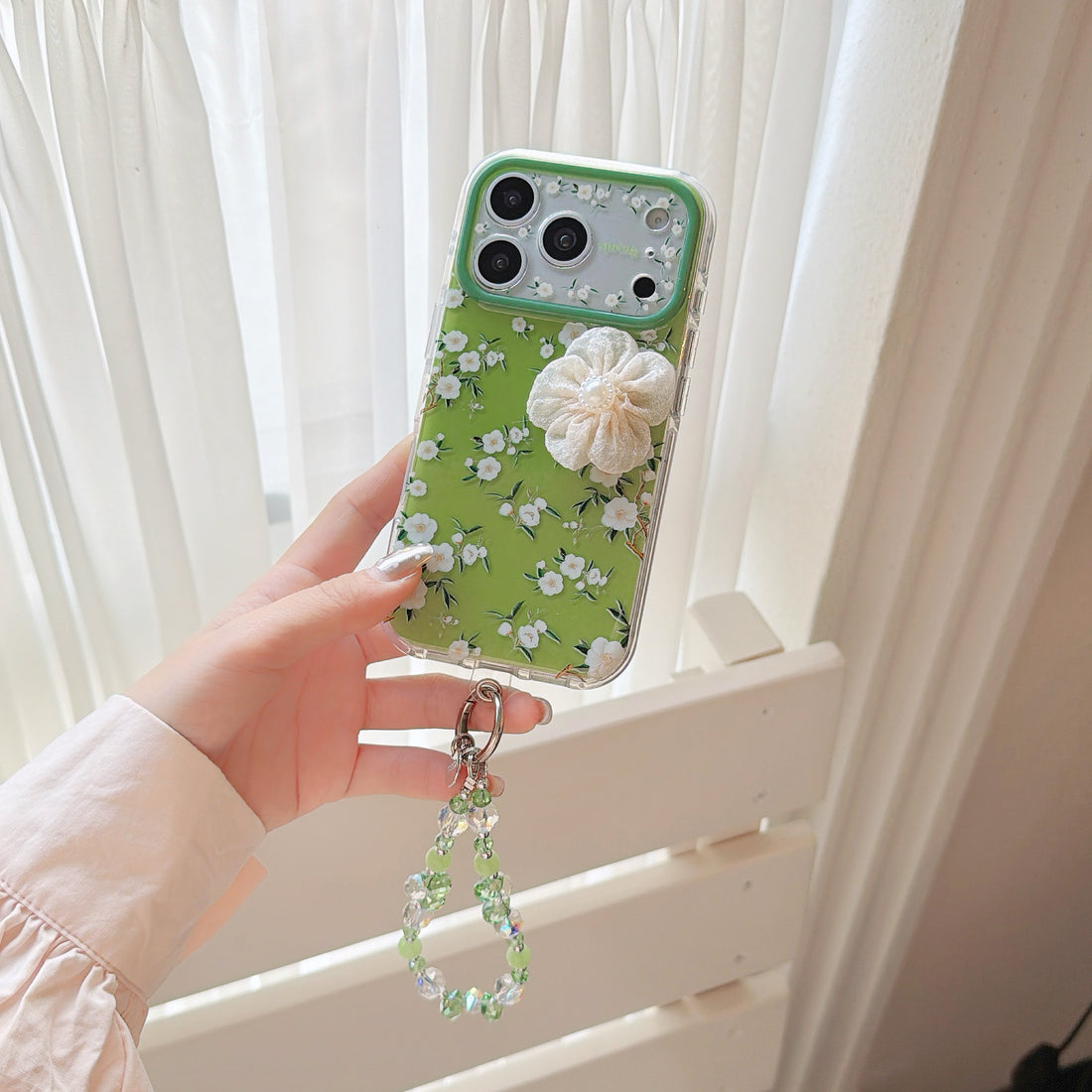 iPhone floral phone case with 3D fabric camellia flower decoration and sparkling beaded strap on clear TPU material with avocado green tint, compatible with iPhone 17/16/15 series